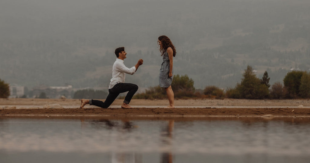 Man proposing to woman barefoot in front of water